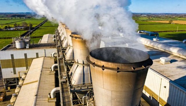 Aerial view showing cooling towers releasing steam at rural industrial plant and farmland