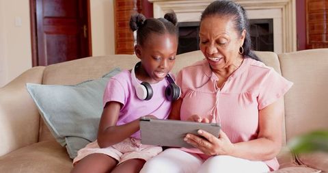 Grandmother and granddaughter bonding over tablet on cozy couch
