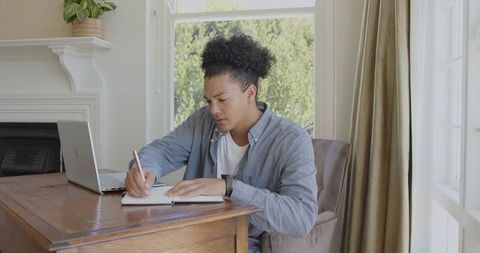Focused young man studying in home office with laptop and notebook