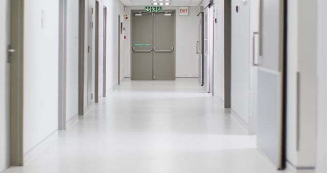 Empty hospital corridor with bright lighting and clear emergency exit signs, evoking a sense of cleanliness and safety. Suitable for healthcare-related articles, advertising, facility management, illustrating concepts of cleanliness and hospital environments.