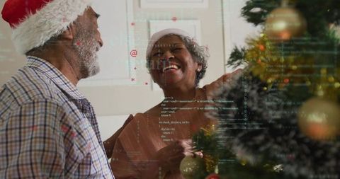 Joyful Couple in Santa Hats Decorating Christmas Tree with Digital Interface