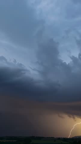 Vertical storm footage showing cumulonimbus sending jagged lightning over farmland at dusk