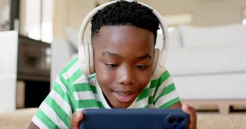 African American boy playing on smartphone with headphones in cozy living room