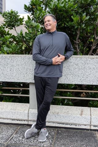Middle-aged man leaning on concrete planter in urban plaza wearing athletic pullover