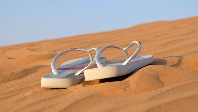 Flip flops lying on a sand dune under a clear blue sky suggest a relaxing summer vacation or desert adventure. Perfect for travel advertisements, vacation planning guides, outdoor adventure blogs, and summer-themed promotions.
