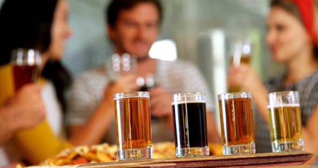 Group of friends enjoying a casual outing at a brewery, tasting different beers from a sampler tray with a variety of drinks. Suitable for topics related to social gatherings, craft beer culture, breweries, friendship, and leisure activities.