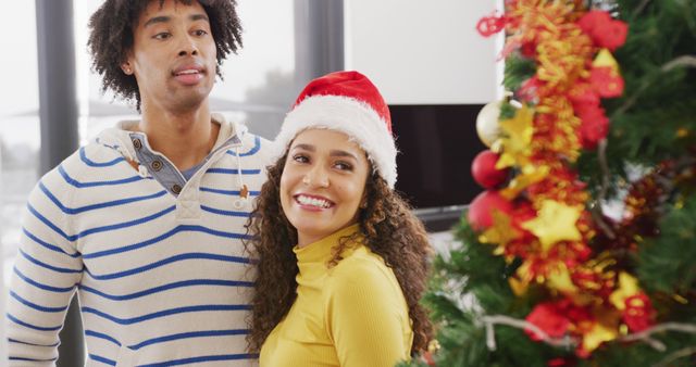 Couple celebrating Christmas, smiling next to beautifully decorated Christmas tree. Image can be used for holiday advertisements, greeting cards, festive promotions, and seasonal blog posts.