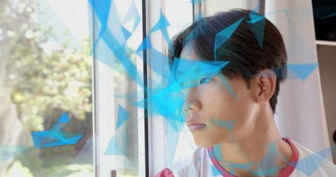 Gazing teenage male by window with blue geometric triangle overlay, contemplative youth