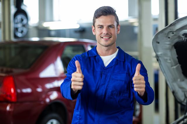Mechanic in blue uniform standing in auto repair shop, smiling and giving thumbs up. Ideal for illustrating automotive services, repair shops, customer satisfaction, and professional mechanics. Can be used in advertisements, websites, and brochures promoting car maintenance and repair services.