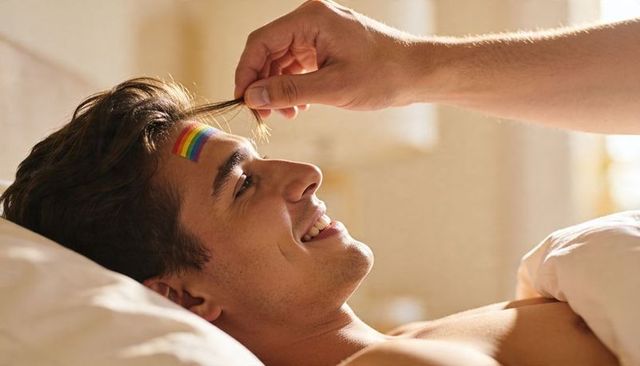 Sunlit morning romance twirling hair of smiling shirtless man with rainbow sticker