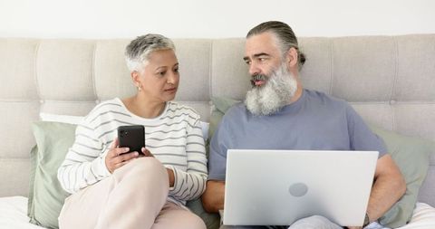 Senior Couple Sharing Technology while Seated on Cozy Bed