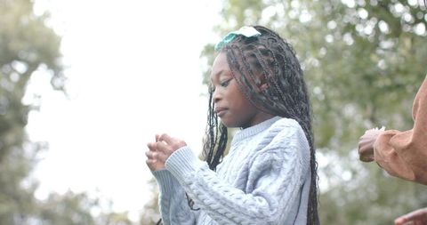 African american girl examining small object outdoors wearing blue sweater and braided hair