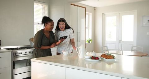 Excited Friends Celebrating News in Sunny Kitchen Gathered Around Tablet