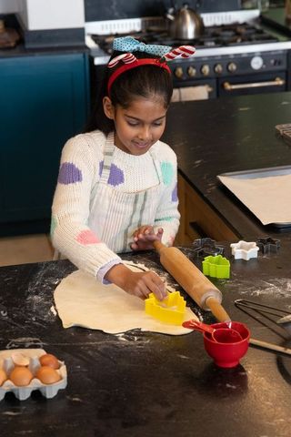 Indian girl pressing cookie cutter into dough while baking cookies in home kitchen