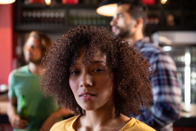 Portrait of biracial woman in a pub during the day, looking at camera her friends in the background. Friendship leisure time fun.