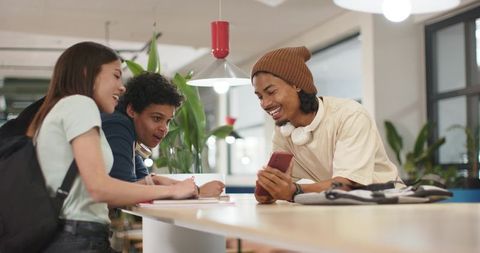 Students collaborating around long table sharing smartphone and notebooks in modern coworking space