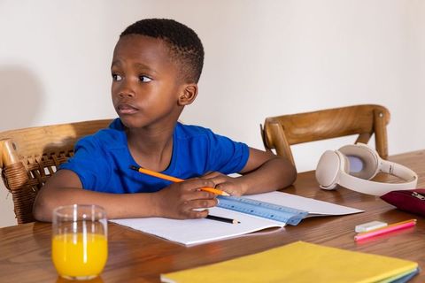 African american boy studying at wooden table with headphones, notebook and orange juice