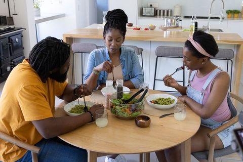 African american family eating green pasta around round table in modern kitchen