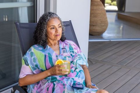 Senior african american woman relaxing on patio with citrus drink in pastel kaftan