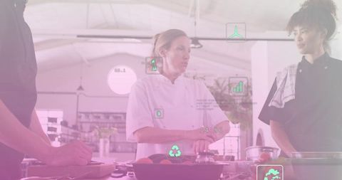 Executive chef mentoring line cook in modern kitchen with digital sustainability icons