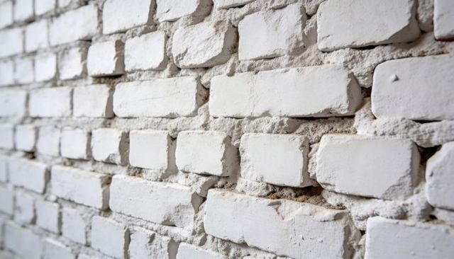 Weathered white brick wall showing textured mortar, flaking paint and chipped edges