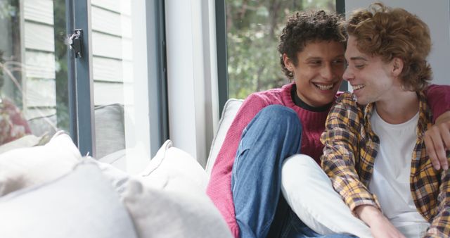 This image captures a happy couple relaxing on a sofa, clearly enjoying their time together indoors. They are smiling and appear affectionate, indicating closeness and warmth. This picture is ideal for use in articles or advertisements about relationships, home life, or emotional well-being. It can also be used in social media posts or campaigns promoting equality, love, and inclusivity.