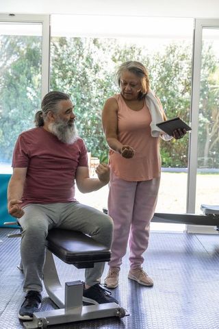 Mature couple exercising in bright home gym using tablet for guided strength training