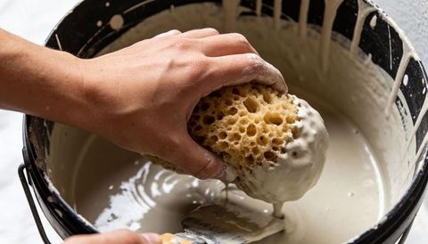 Hand squeezing porous sponge into plaster bucket, dripping paste, trowel in frame