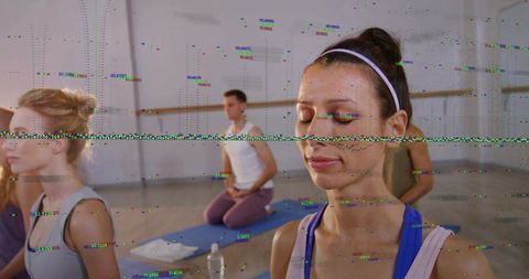 Woman meditating in group yoga class on blue mat wearing white headband and tank top