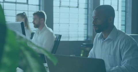 Focused professional typing on laptop in modern open-plan office with natural daylight