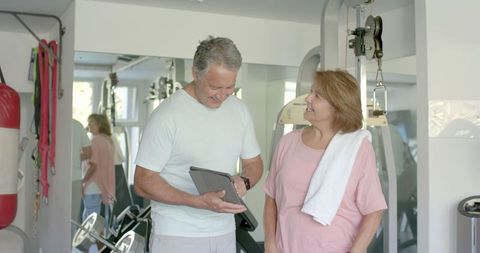 Senior couple discussing fitness routine with tablet in home gym