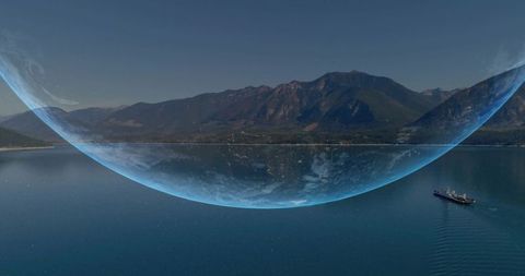 Giant Translucent Orb Arching Over Mountain Coastline with Freighter Crossing Calm Reflective Water