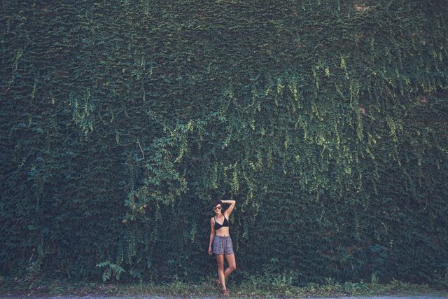 Woman standing and posing confidently against a backdrop of a lush green ivy-covered wall. This dynamic and vibrant image can be used in fashion, lifestyle, outdoor adventure articles, marketing campaigns, or social media posts to evoke a sense of nature, confidence, and style.