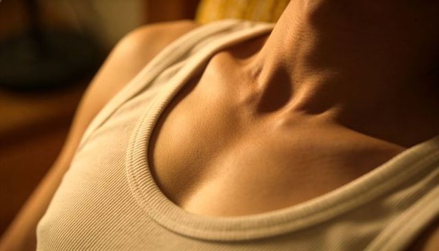Reclining silhouette showing glowing collarbone and neckline in white ribbed tank top
