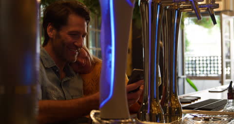 Couple Enjoying Leisure Time at Hotel Bar Using Smartphone