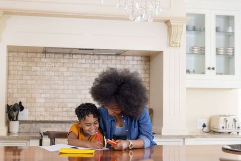 African american mother helping son with homework at kitchen island, cozy family learning