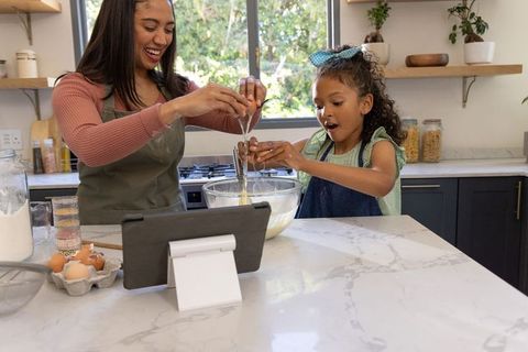 Mother and daughter baking together in bright kitchen following tablet recipe, joyful