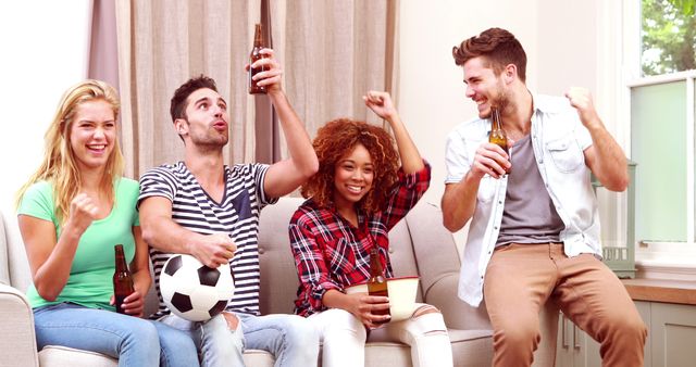 Group of young friends enjoying a soccer match at home, holding drinks and cheering enthusiastically. Ideal for concepts of friendship, celebration, sports fans, casual gatherings, and home entertainment.
