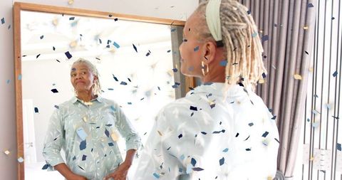 Confetti celebration featuring stylish senior woman admiring mirror reflection in bedroom