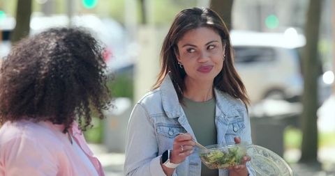 Multiracial friends chatting outdoors while woman in denim jacket eating salad