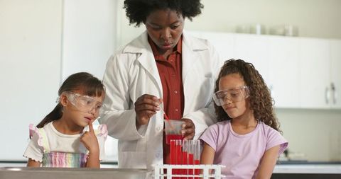African American teacher demonstrating colorful chemistry experiment with teen girls in lab