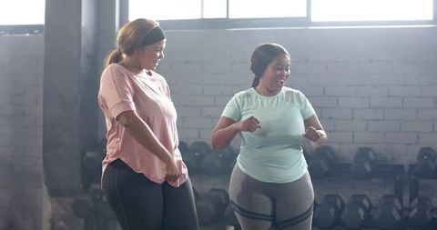 Plus-size diverse women chatting and laughing during strength training near dumbbells