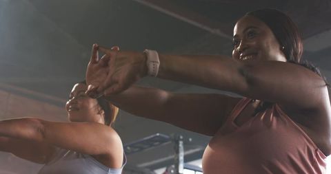 Diverse women stretching together in gym class wearing tanks and smartwatch for fitness
