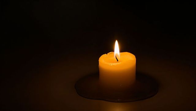 Short yellow candle glowing warmly with flickering flame and glossy melted wax pool