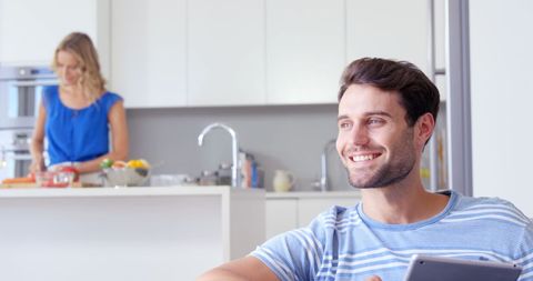 Happy Man Using Tablet While Partner Prepares Meal in Modern Kitchen - Download Free Stock Images Pikwizard.com