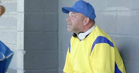 Mature baseball player sitting in dugout wearing yellow blue jersey cap with headphones