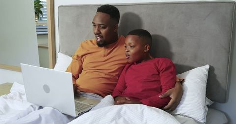 Father and son bonding with technology in cozy bedroom