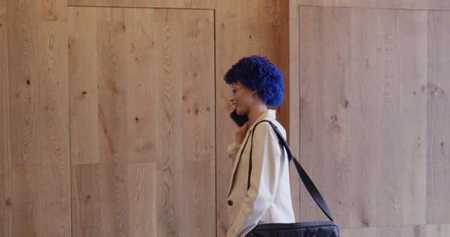 Profile of happy biracial casual businesswoman with blue afro talking on smartphone in office. Casual office, business, communication and work, unaltered.