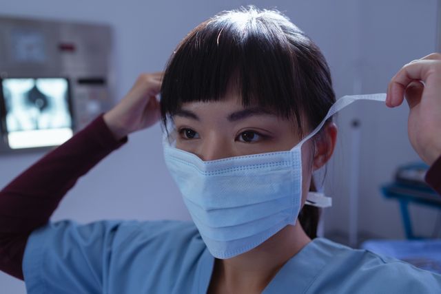 Female surgeon adjusting surgical mask in a hospital operation room. Ideal for use in healthcare, medical, and hospital-related content, including articles, websites, and educational materials about medical professionals, surgical procedures, and patient care.