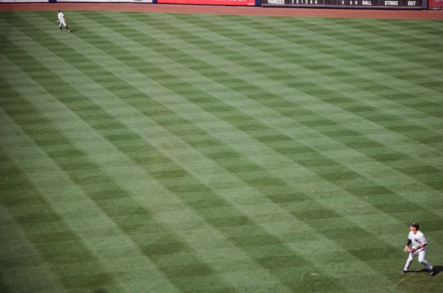 Outfielders maintaining position on a neatly mowed grass field during a baseball game. This can be used in sports blogs, articles about baseball, or promotional materials for baseball leagues and tournaments.